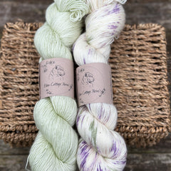 Two skeins of yarn - one pale green, one cream with green, purple and brown splashes