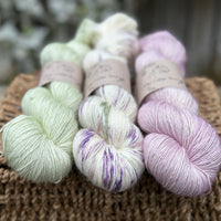 Three skeins of yarn. From left to right: a pale green skein, a cream skein with purple, green and brown splashes, a pale pink skein
