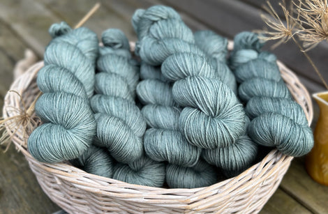 A white wicker basket containing several skeins of blue/green yarn