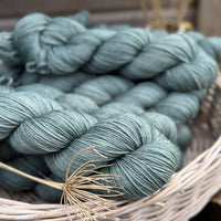 A white wicker basket containing several skeins of blue/green yarn