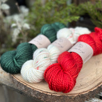 Three skeins of yarn. From left to right: a dark green skein, a cream skein with green and red speckles and a bright red skein