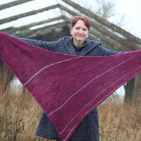 Victoria holding a purpley pink triangular shawl outstretched. The shawl has stripes in muted contrast colours