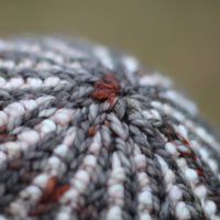 The crown of a two tone beanie hat in cream and beige with a dark grey and red contrast