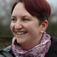 Victoria wearing a grey jacket and a variegated pink and purple cowl with a single cable up the front.