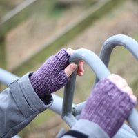 A person holding a metal fence and wearing purple fingerless mitts