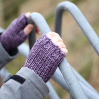 A person holding a metal fence and wearing purple fingerless mitts