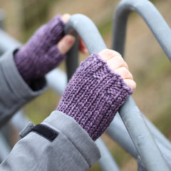 A person holding a metal fence and wearing purple fingerless mitts