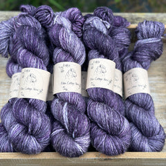 Skeins of variegated purple, grey and cream yarn with white slubs running through them