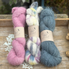 Three skeins of fluffy laceweight yarn in shades of pink, blue and cream