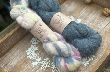 Two skeins of fluffy laceweight yarn - one variegated cream skein with multicoloured splashes and one with dark blue skein