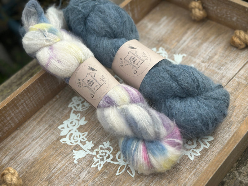 Two skeins of fluffy laceweight yarn - one variegated cream skein with multicoloured splashes and one with dark blue skein