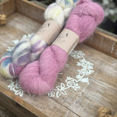 Two skeins of fluffy laceweight yarn - one variegated cream skein with multicoloured splashes and one pink skein