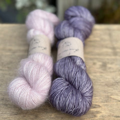 Two skeins of yarn - one is a pink fluffy laceweight skein and the other is a purple skein.