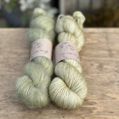 Two skeins of green yarn - one is a fluffy laceweight skein.
