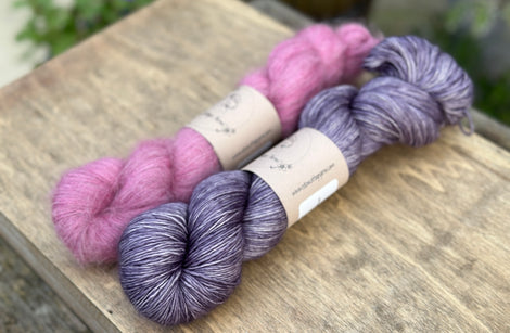 Two skeins of yarn - one pink fluffy laceweight skein and one purple skein