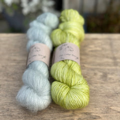 Two skeins of yarn - one pale blue fluffy laceweight skein and one zingy green skein