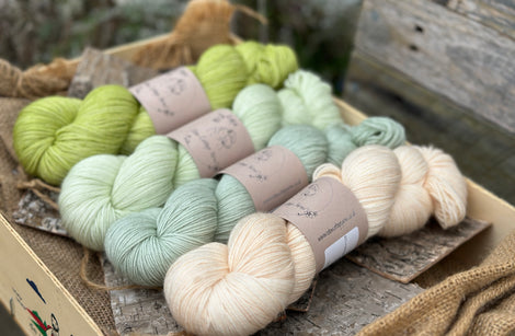 Four skeins of yarn in shades of green and cream