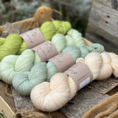 Four skeins of yarn in shades of green and cream