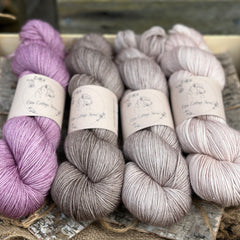 Four skeins of yarn. From left to right: a purple skein, a mid grey brown skein, a light brown skein and a beige skein