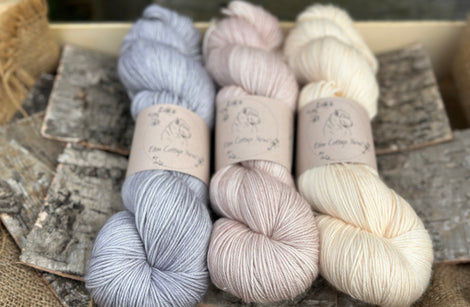 Three skeins of yarn. From left to right: a blue-grey skein, a beige skein and a cream coloured skein