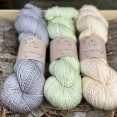 Three skeins of yarn. From left to right: a blue-grey skein, a pale green skein and a pale orange skein