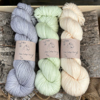 Three skeins of yarn. From left to right: a blue-grey skein, a pale green skein and a pale orange skein