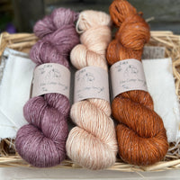 Three skeins of hand dyed yarn in soft lilacy pink, light warm cream, and rust orange.