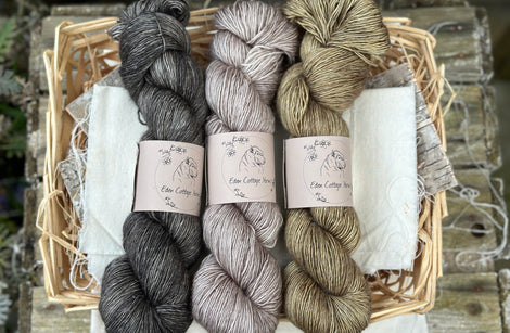 Three skeins of yarn. From left to right: a dark grey skein, a grey brown skein and a brownish green skein