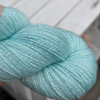 Close up image of a skein of pale blue yarn with silver stellina running through it