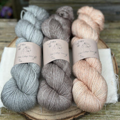 Three skeins of yarn with silver sparkle running through it. From left to right: a grey skein, a mid-brown skein and a pale orange skein