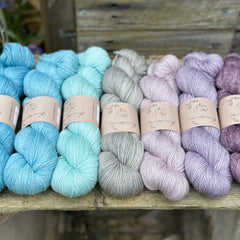 Seven skeins of yarn with silver sparkle running through it. The colours fade from blue on the left to grey in the middle and purple on the right