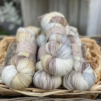 Four skeins of variegated cream, grey, brown and beige yarn with gold sparkle running through it