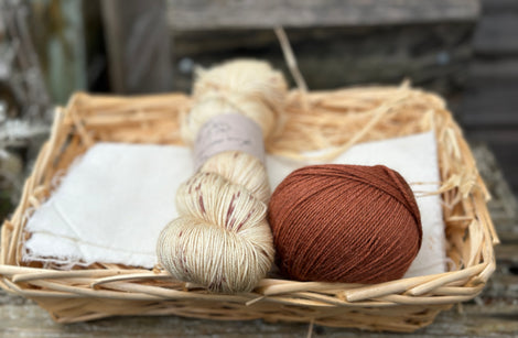 A skein of beige yarn with reddish brown speckles with a ball of reddish brown yarn