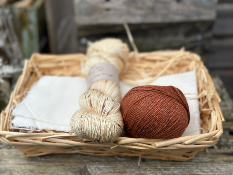 A skein of beige yarn with reddish brown speckles with a ball of reddish brown yarn