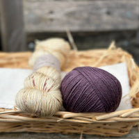 A skein of beige yarn with purple speckles with a ball of purple yarn