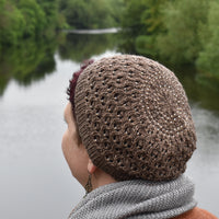 A person wearing a brown knitted hat is looking out over a lake. The hat includes a lace pattern and beads throughout