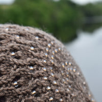 Close up detail of a knitted brown hat with a lace pattern and beads