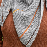A close up image of a triangular grey shawl. The shawl is grey with thin stripes of contrasting colours