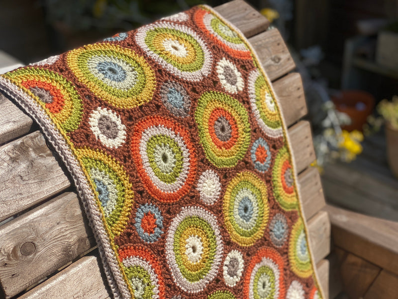 A crocheted rectangular wrap which has an all-over motif of multicoloured circles.