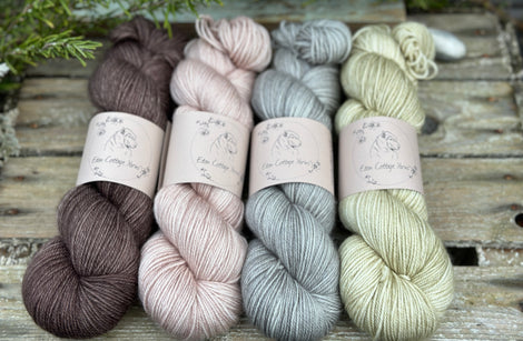 Four skeins of yarn. From left to right: a brown skein, a beige skein, a grey skein and a pale green skein