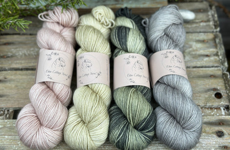 Four skeins of yarn. From left to right: a beige skein, a pale green skein, a variegated green skein and a grey skein