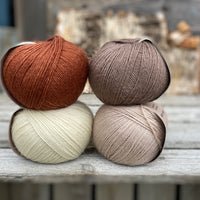Four balls of yarn. Colours are natural cream, beige, reddish brown and brown
