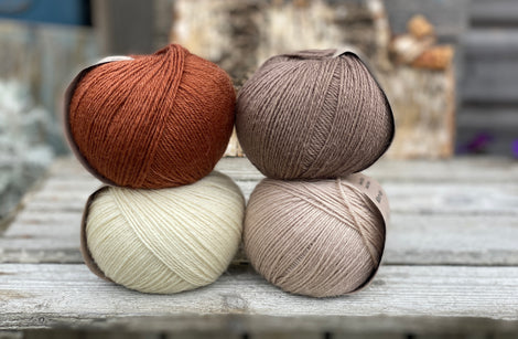 Four balls of yarn. Colours are natural cream, beige, reddish brown and brown
