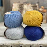 Four balls of yarn. Colours are pale blue, blue, yellow and dark blue