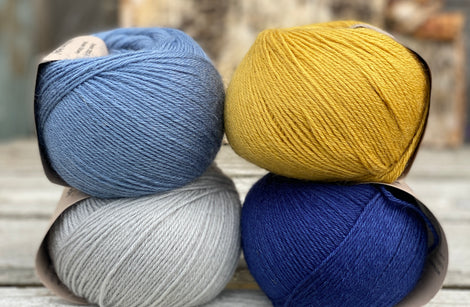 Four balls of yarn. Colours are pale blue, blue, yellow and dark blue