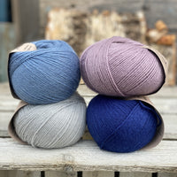 Four balls of yarn. Colours are pale blue, blue, pale purple and dark blue