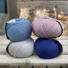 Four balls of yarn. Colours are pale blue, blue, pale purple and dark blue