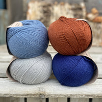 Four balls of yarn. Colours are pale blue, blue, reddish brown and dark blue