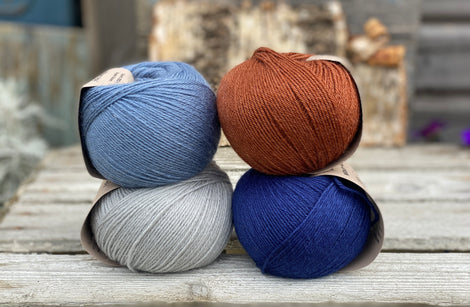 Four balls of yarn. Colours are pale blue, blue, reddish brown and dark blue