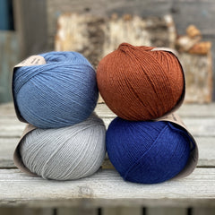 Four balls of yarn. Colours are pale blue, blue, reddish brown and dark blue